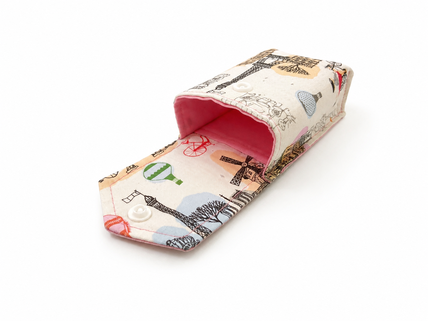 A fabric eyeglasses case with a Paris-themed print featuring Eiffel Towers, windmills, and hot air balloons on a cream background, with a bright pink interior lining and a snap button closure.